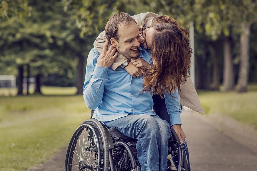 woman wrapping her arms around boyfriend in wheelchair in the city park